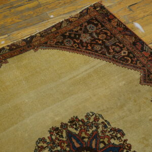 A corner view of a beige rug with a dark border on worn wood plank flooring.