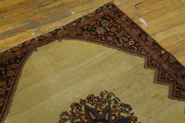 A corner view of a beige rug with a dark border on worn wood plank flooring.