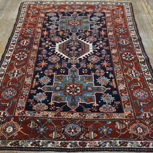 Navy blue and rust red geometric patterned rug displayed on light-colored wood planks.