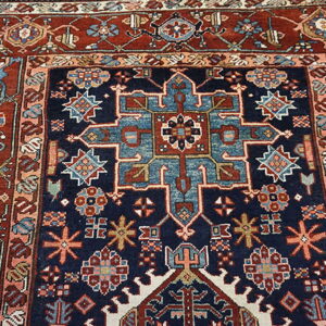 Traditional geometric rug in navy, rust, and light blue with central medallions shown on wood floors.