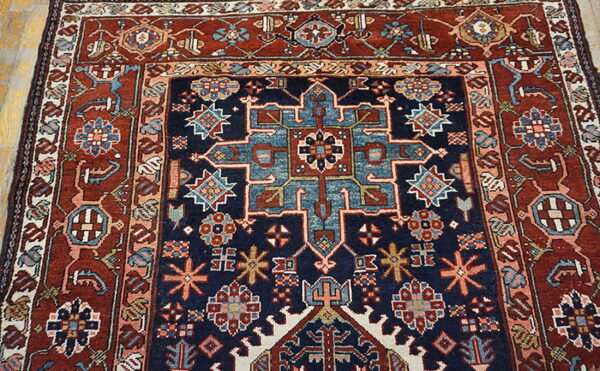 Traditional geometric rug in navy, rust, and light blue with central medallions shown on wood floors.