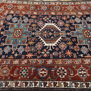 Navy blue and red geometric rug with a central medallion and tribal motifs on light wood floors.