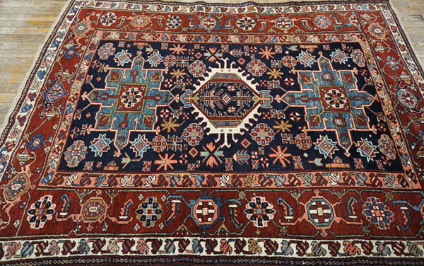 Navy blue and red geometric rug with a central medallion and tribal motifs on light wood floors.