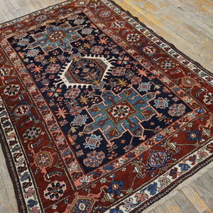 Geometric area rug in navy and brick red with stylized motifs on light gray wood flooring.