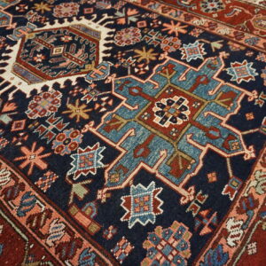 Detailed view of a rug showing a navy blue field with teal, rust, and cream geometric tribal patterns.