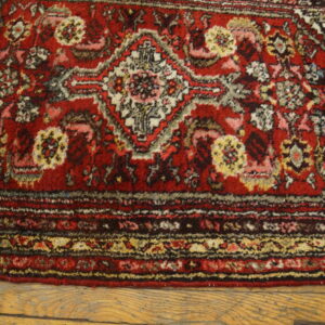 Dark red traditional rug featuring complex floral and geometric motifs resting on light wood flooring.