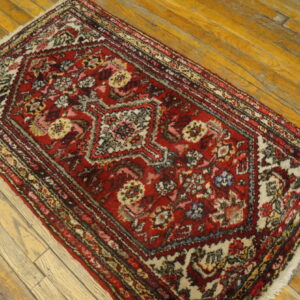 Low-pile red rug with complex medallion pattern and white fringe lays across distressed wooden floorboards.
