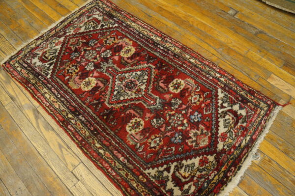 Low-pile red rug with complex medallion pattern and white fringe lays across distressed wooden floorboards.