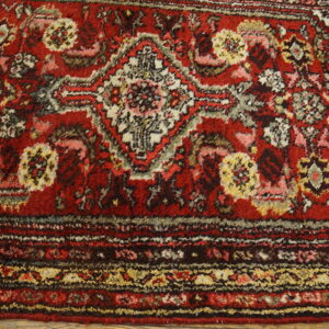 Red high-pile rug detail showing complex traditional patterns, multicolored medallions, and a decorative border.