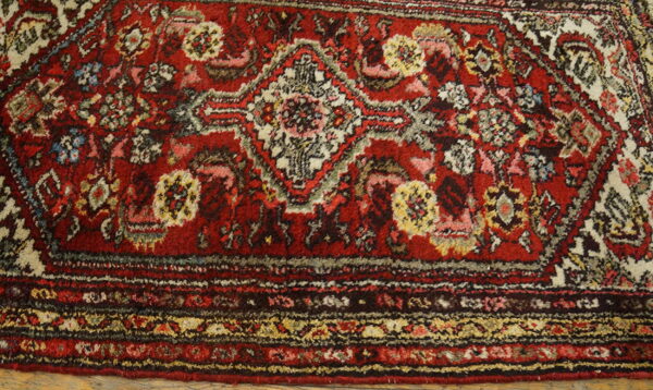 Red high-pile rug detail showing complex traditional patterns, multicolored medallions, and a decorative border.