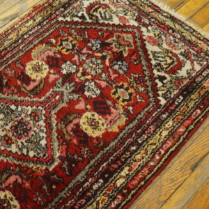 Red and white traditional rug with dense floral patterns and fringe on distressed light wood flooring.