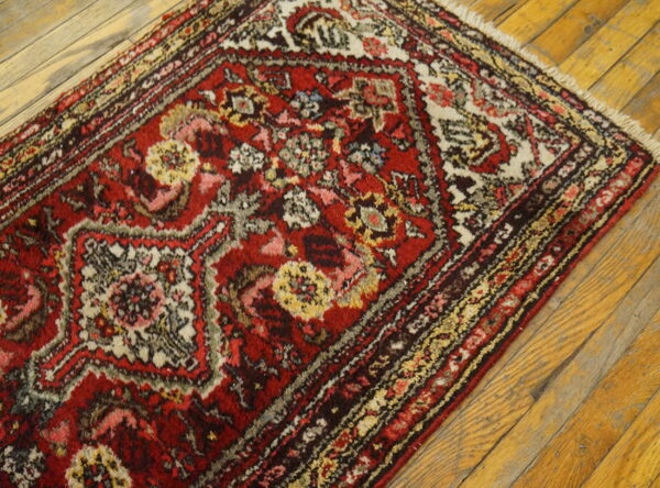 Red and white traditional rug with dense floral patterns and fringe on distressed light wood flooring.