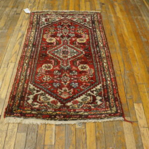Small red and multicolored traditional rug with fringe on distressed wood plank flooring.