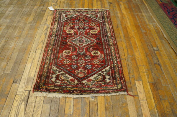 Small red and multicolored traditional rug with fringe on distressed wood plank flooring.
