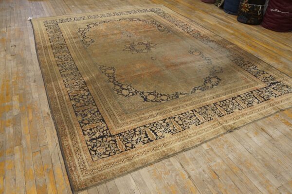 A large, worn traditional area rug with dark floral designs displayed on distressed wood planks.