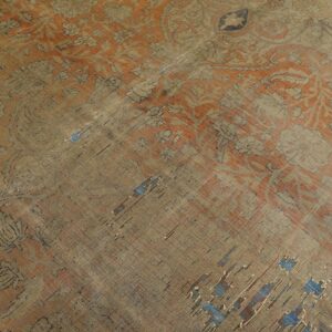 The heavily worn orange and beige rug features a traditional pattern and exposed blue foundation threads.