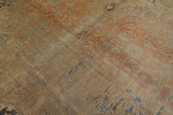 The heavily worn orange and beige rug features a traditional pattern and exposed blue foundation threads.