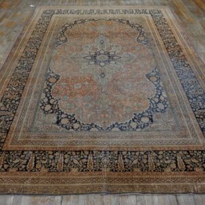 Large orange and navy medallion rug with a detailed border lies on wide distressed wooden floorboards.