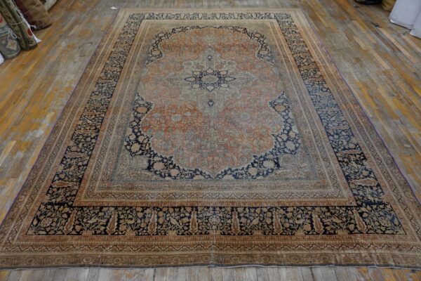 Large orange and navy medallion rug with a detailed border lies on wide distressed wooden floorboards.