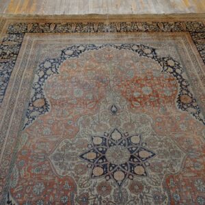 Ornate terracotta and navy rug with a central arched field and borders on distressed wood planks.