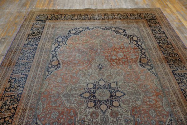Ornate terracotta and navy rug with a central arched field and borders on distressed wood planks.
