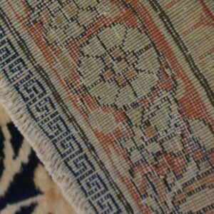 Floral pile rug with navy and tan colors rests next to the woven geometric backing of a second rug.