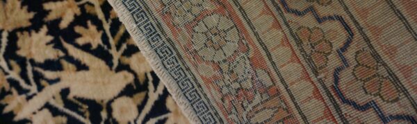 Floral pile rug with navy and tan colors rests next to the woven geometric backing of a second rug.