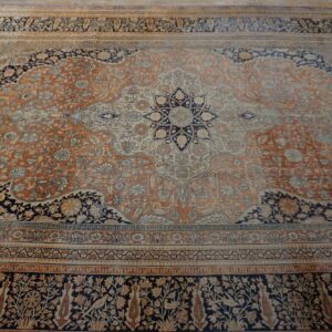 Ornate traditional rug with a rust orange and cream field, navy accents, and complex floral borders.