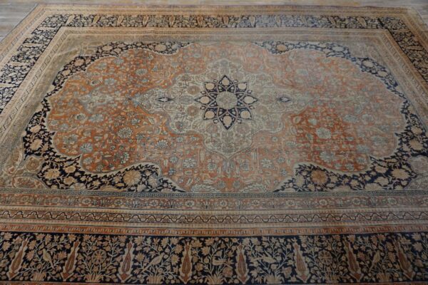 Ornate traditional rug with a rust orange and cream field, navy accents, and complex floral borders.