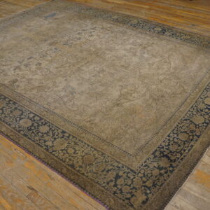 Worn beige and navy large rug with floral motifs displayed on rustic, wide plank wood floors.