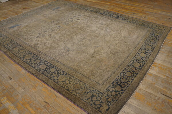 Worn beige and navy large rug with floral motifs displayed on rustic, wide plank wood floors.
