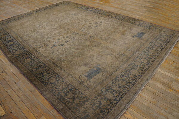 Low-pile, faded tan rug featuring blue floral patterns and a dark ornamental border on wood flooring.