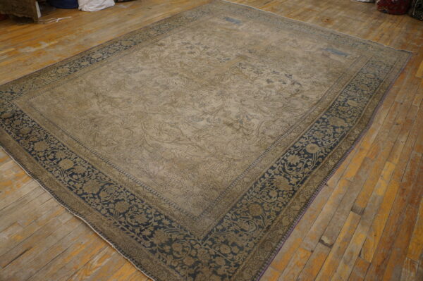 Light beige low-pile rug with a detailed floral pattern and dark navy border on rustic wood planks.