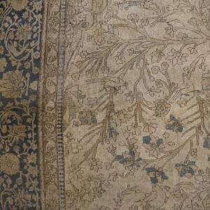 Close up of a low pile rug featuring beige, brown, and blue floral motifs bordered by dark blue on wood.