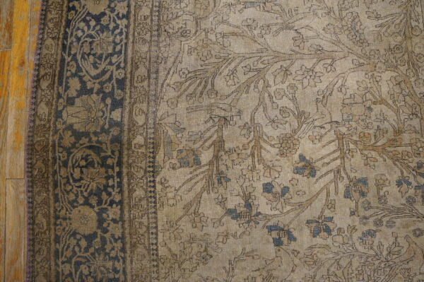 Close up of a low pile rug featuring beige, brown, and blue floral motifs bordered by dark blue on wood.