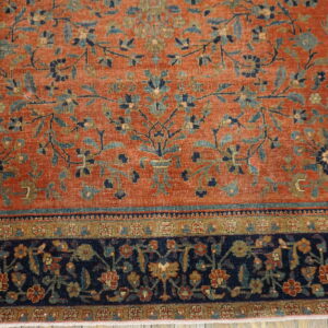 Rust-colored low-pile rug with a detailed blue, teal, and gold botanical pattern and a dark navy border.