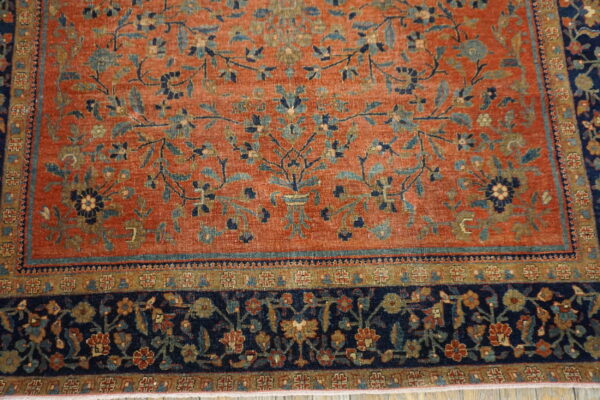 Rust-colored low-pile rug with a detailed blue, teal, and gold botanical pattern and a dark navy border.