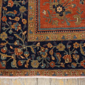 Close-up of a rug corner featuring intricate navy, rust, gold, and teal floral patterns resting on distressed wooden flooring.