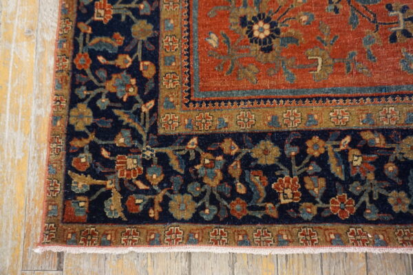 Close-up of a rug corner featuring intricate navy, rust, gold, and teal floral patterns resting on distressed wooden flooring.