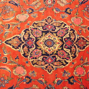 Close-up of a rug featuring an orange field with a navy blue medallion and elaborate floral motifs.