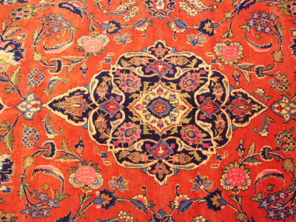 Close-up of a rug featuring an orange field with a navy blue medallion and elaborate floral motifs.