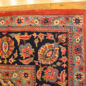 Traditional navy rug corner with red and blue floral patterns on light plank hardwood flooring.