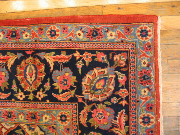 Traditional navy rug corner with red and blue floral patterns on light plank hardwood flooring.