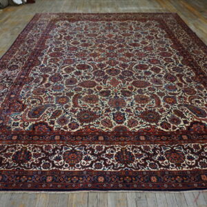Low-pile rug with a detailed cream, red, and blue floral design covers a distressed wood floor.