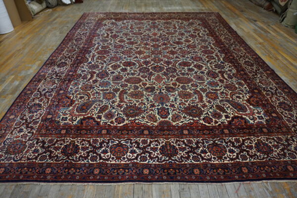 Low-pile rug with a detailed cream, red, and blue floral design covers a distressed wood floor.