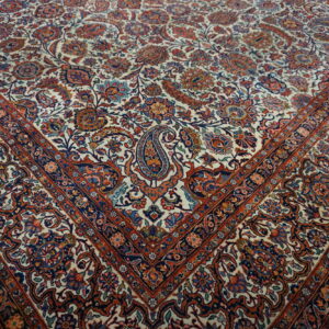 Floral patterned rug with a cream field, navy and rust accents, lying on light wooden floorboards.