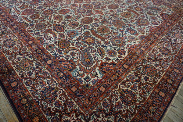 Floral patterned rug with a cream field, navy and rust accents, lying on light wooden floorboards.