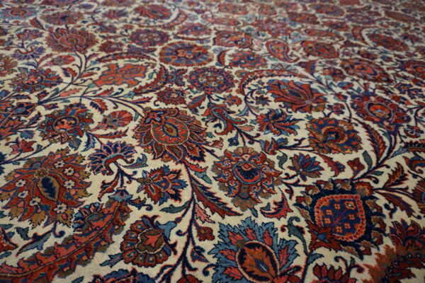 Detailed view of a low-pile rug with dense floral patterns in cream, deep blue, and terracotta red.