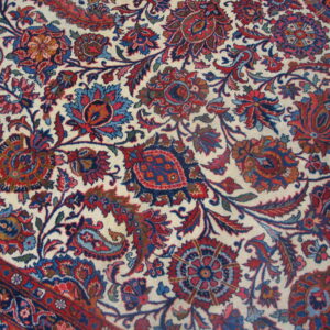 Intricate red and blue floral pattern on a cream field, showing a corner section and the multi-banded border.