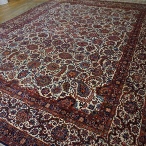 Large traditional ivory rug with dense red and blue floral patterns covers a worn wood plank floor.